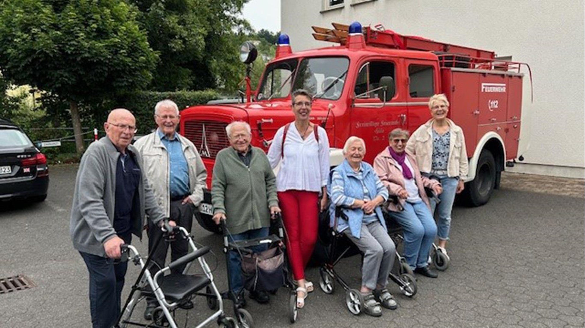 Gäste der Tagespflege stellen sich vor dem Feuerwehrauto zum Gruppenbild auf