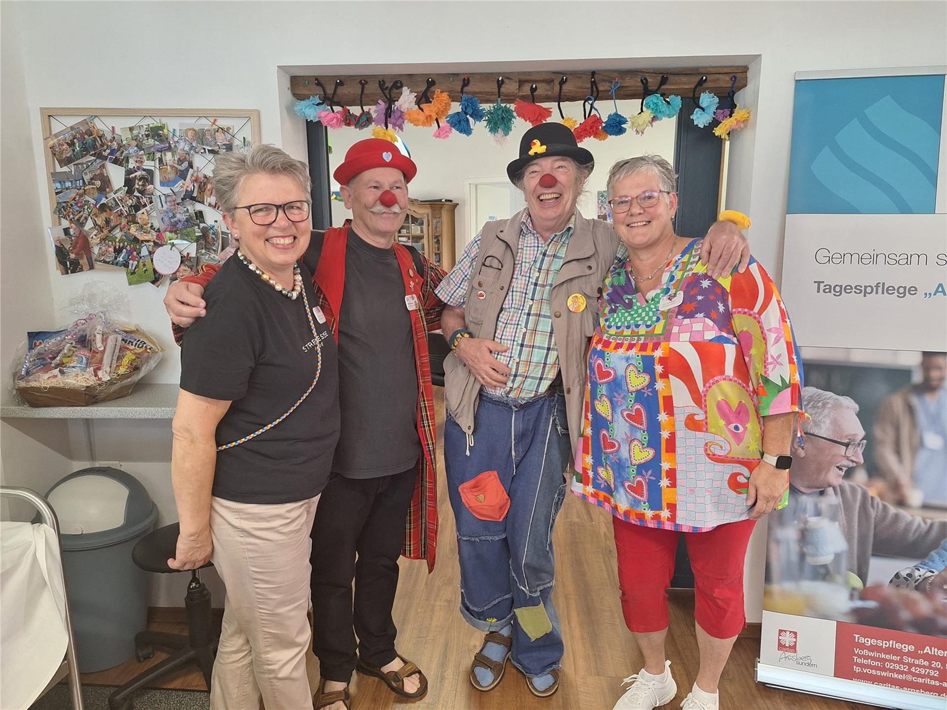Zwei Mitarbeitende stehen gemeinsam mit zwei Clowns und lachen in die Kamera. Der Besuch sorgt für gute Stimmung in der Tagespflege.