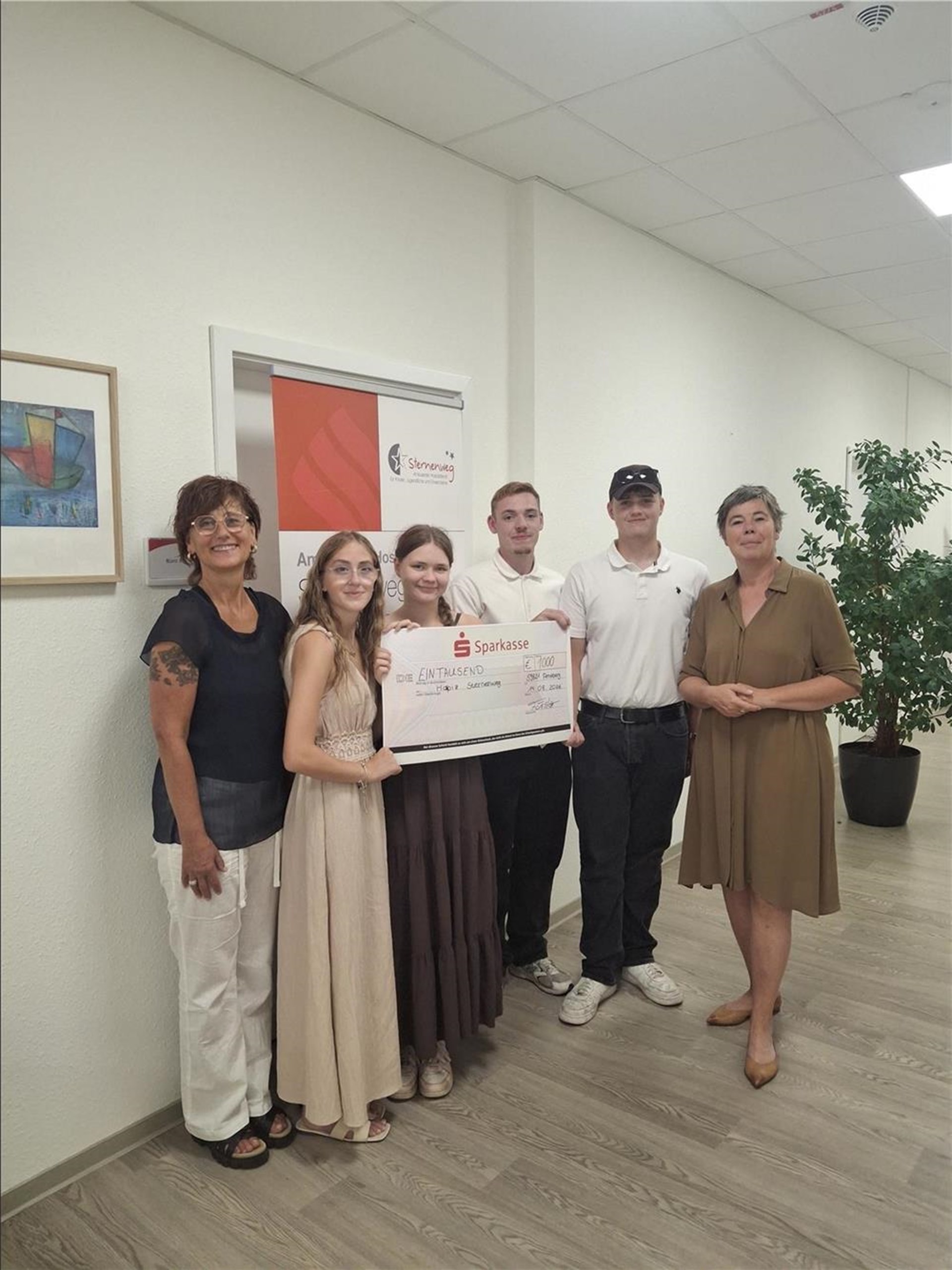 Eine Gruppe aus Schülerinnen und Schülern sowie Vertreterinnen des Ambulanten Hospizdienstes Sternenweg hält gemeinsam einen symbolischen Spendenscheck über 1.000 Euro und freut sich über die Unterstützung.