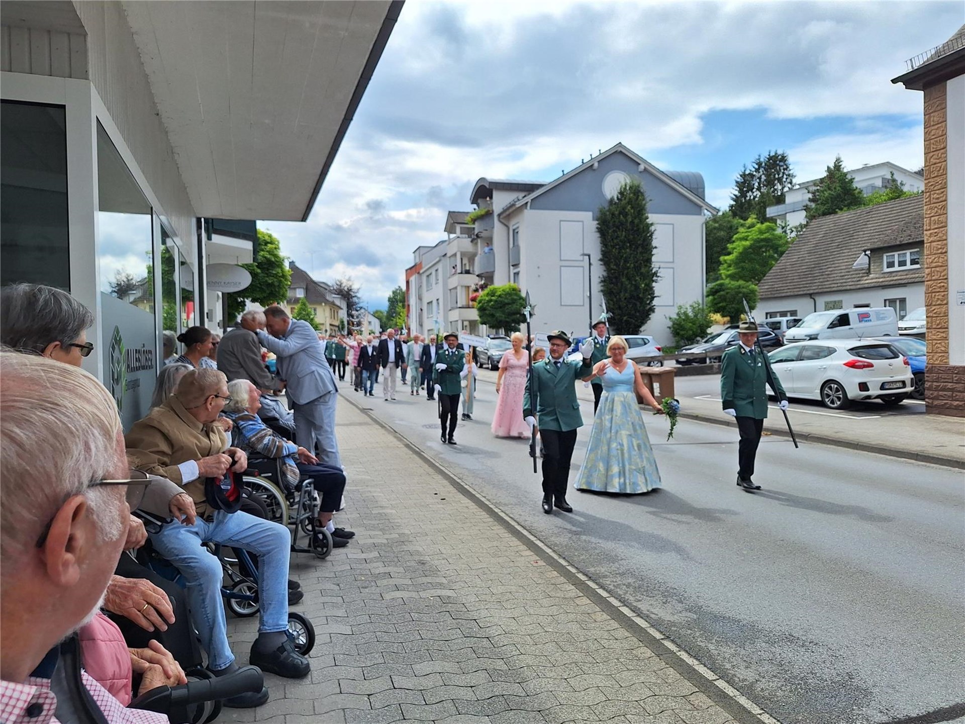 Bewohner verfolgen vom Straßenrand aus einen festlichen Schützenumzug mit Schützenpaaren und zahlreichen Teilnehmenden.