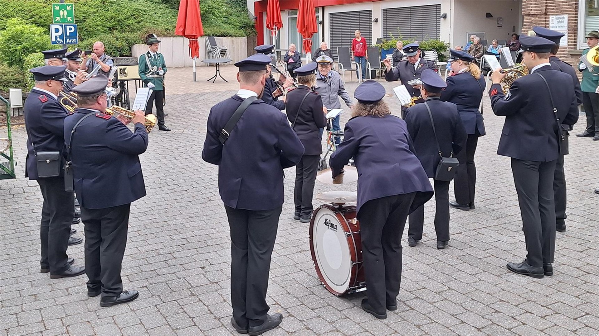 Musiker in Uniformen eines Spielmannszugs stehen vor dem Gebäude des Seniorenhauses und bringen ein Ständchen. 