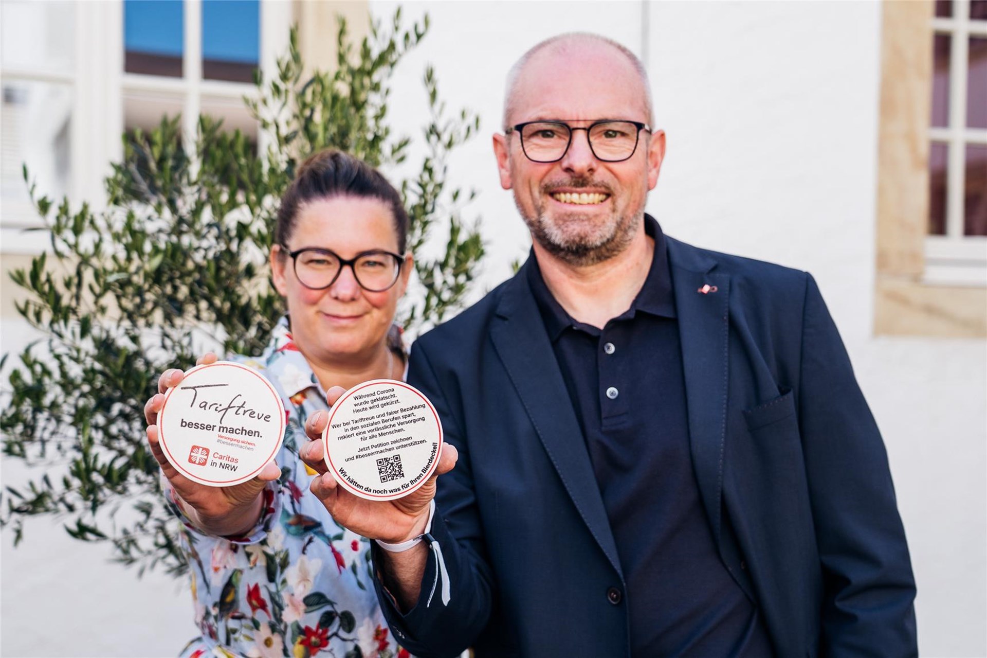 Esther van Bebber und Ralf Nolte halten jeweils einen Bierdeckel in Händen mit der Aufschrift "Tariftreue. besser machen". 