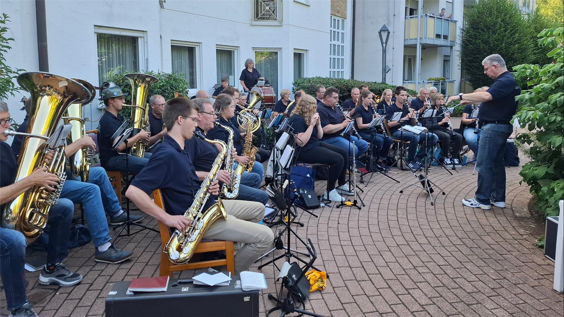 Die Musiker und Musikerinnen des Musikvereins Langenholthausen sitzen mit ihren Instrumenten im Garten des Seniorenhauses und geben ein Konzert. Zu sehen sind Personen Tuba, Posaune, Horn, Saxophon, Klarinetten usw. 