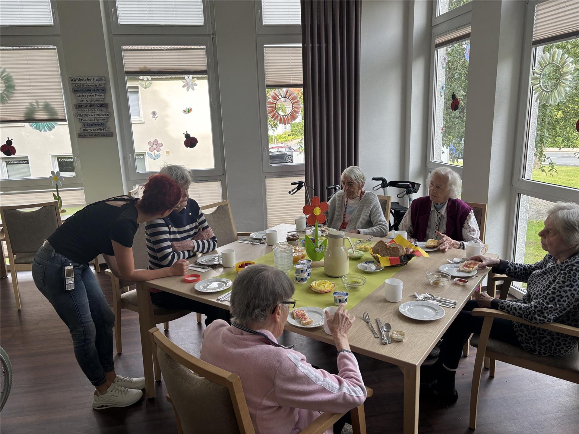 Gemeinsames Frühstück in der Tagespflege: Mitarbeitende und Seniorinnen sitzen zusammen am liebevoll gedeckten Tisch und genießen die gemeinsame Zeit.